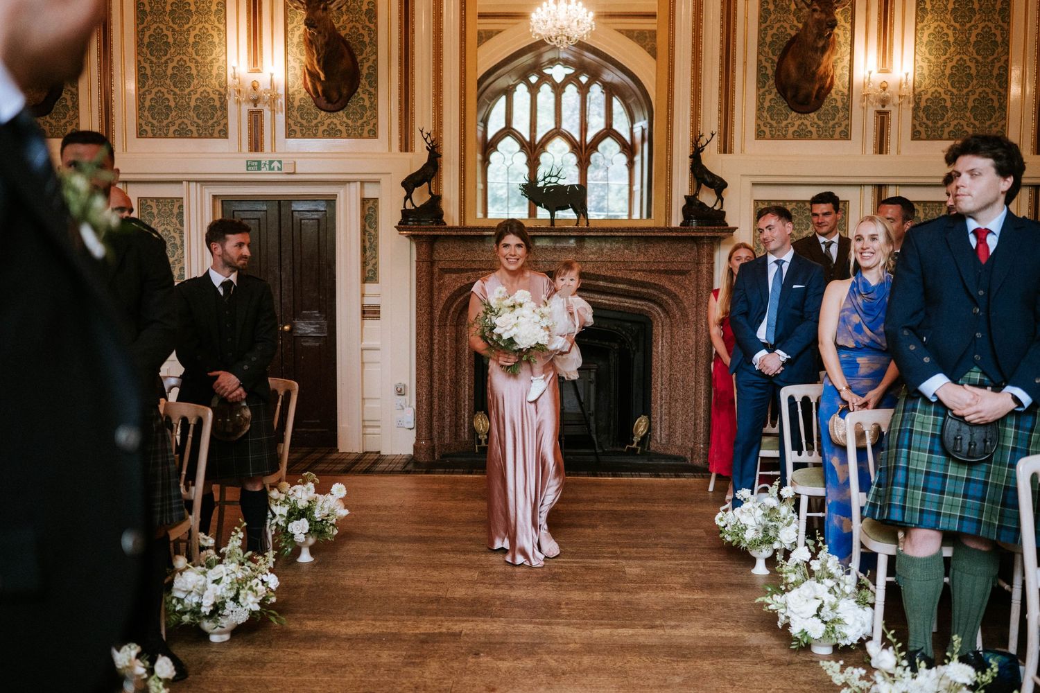 Elegant wedding ceremony setup in a grand hall with white floral arrangements and candle lighting.