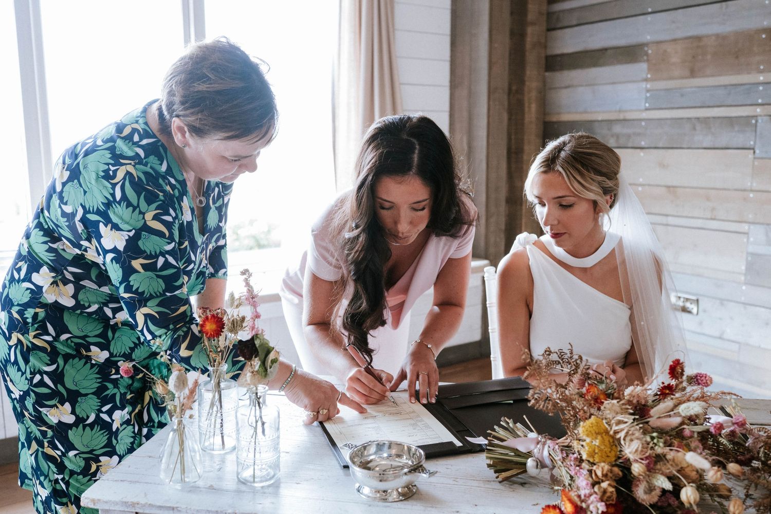 Wedding preparation scene with group gathered around table with flowers.