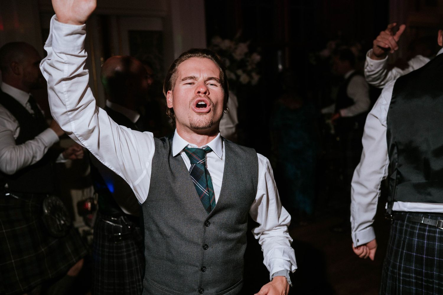 Wedding party guests dancing enthusiastically in formal attire.