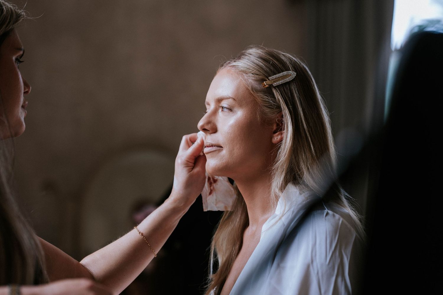 A bride getting ready in front of a window with natural light streaming in.