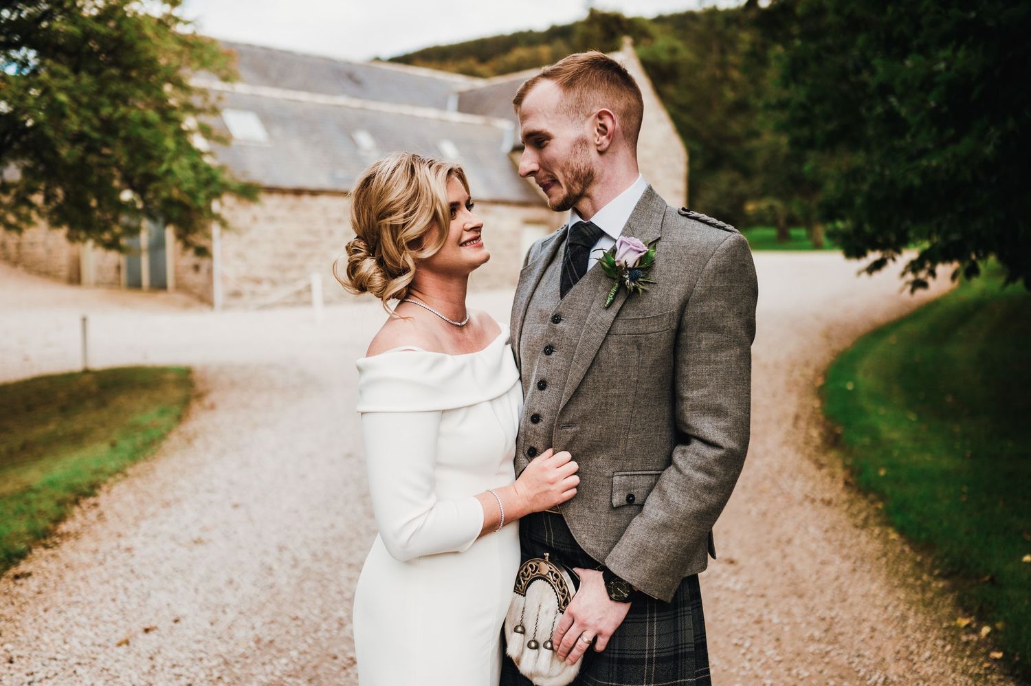 Romantic countryside wedding photos on gravel path with green fields in background.