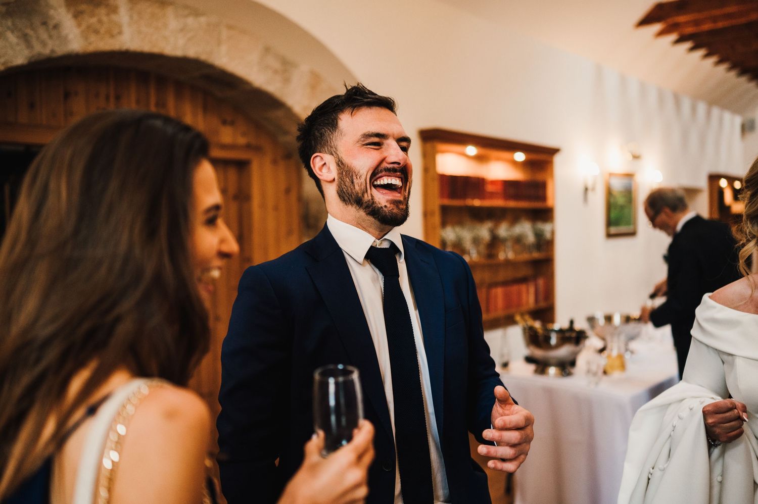 Wedding reception guests mingling and socializing in an elegant indoor venue with warm lighting.