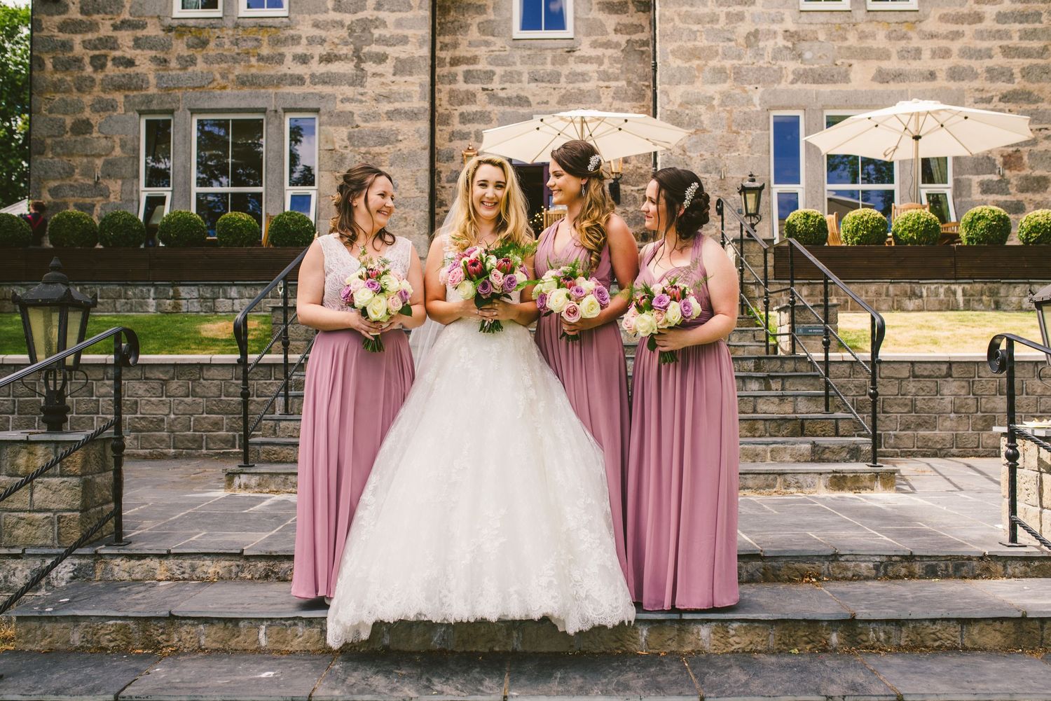 Large wedding party gathered outside stone building for formal photographs.