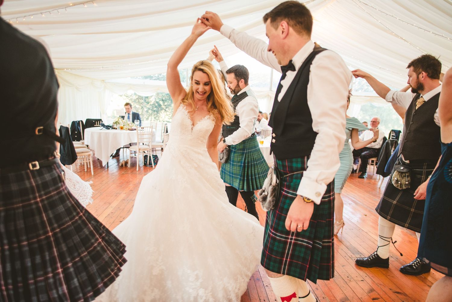 Wedding celebration features traditional Scottish dancing with kilts and white dress in marquee tent.