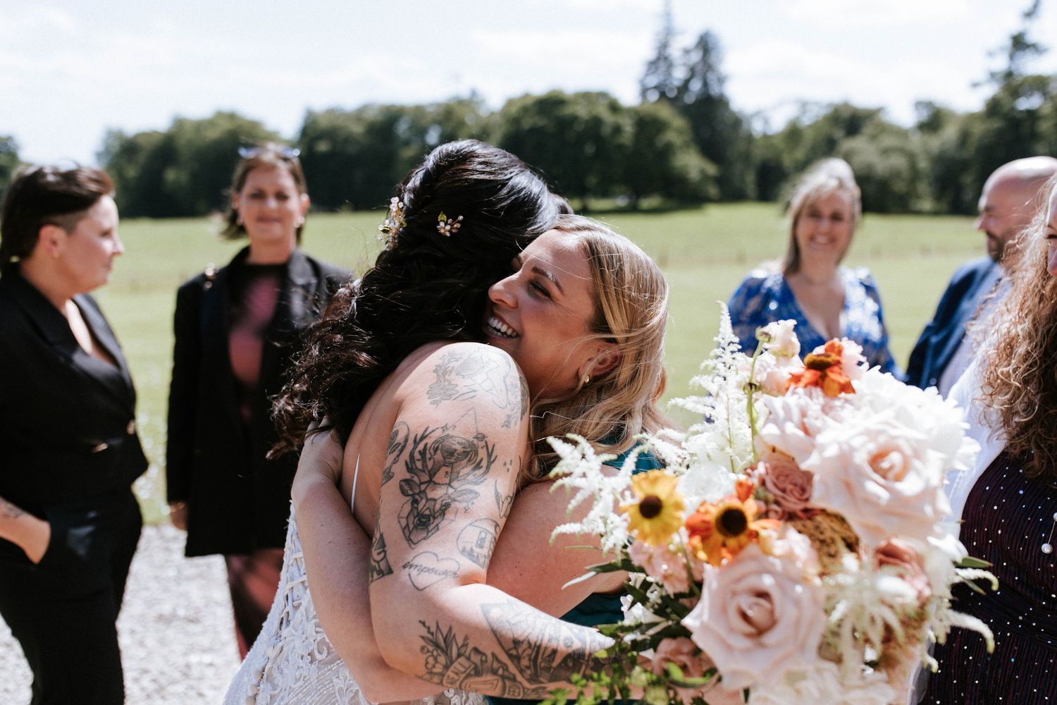 Wedding party mingles and celebrates on sunny lawn with floral arrangements.