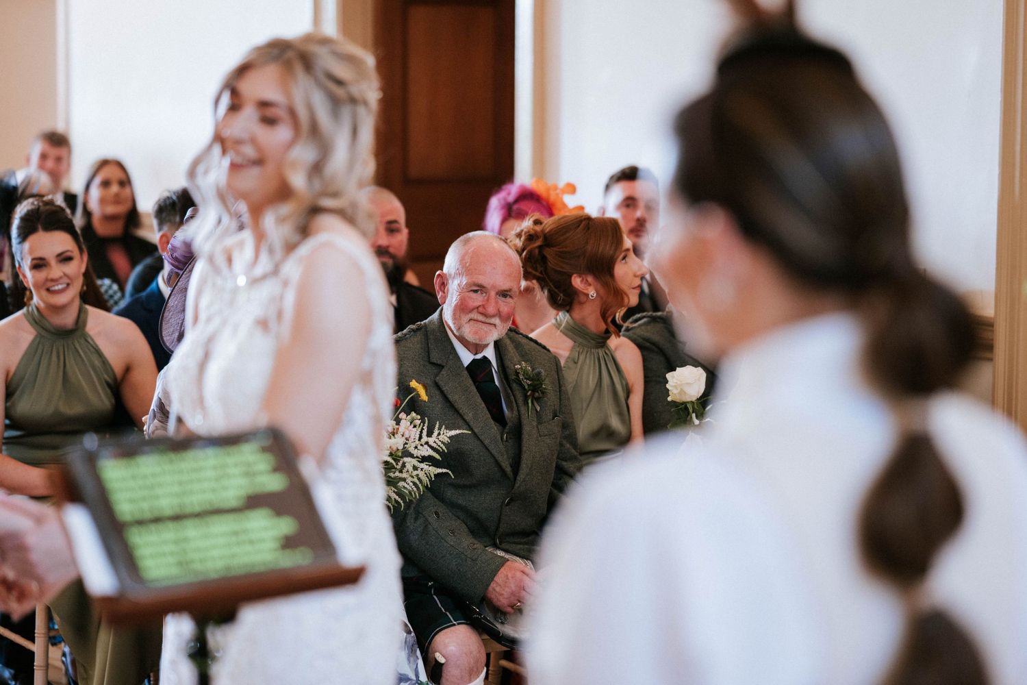 Guests observe a wedding ceremony in a bright indoor venue with white walls.