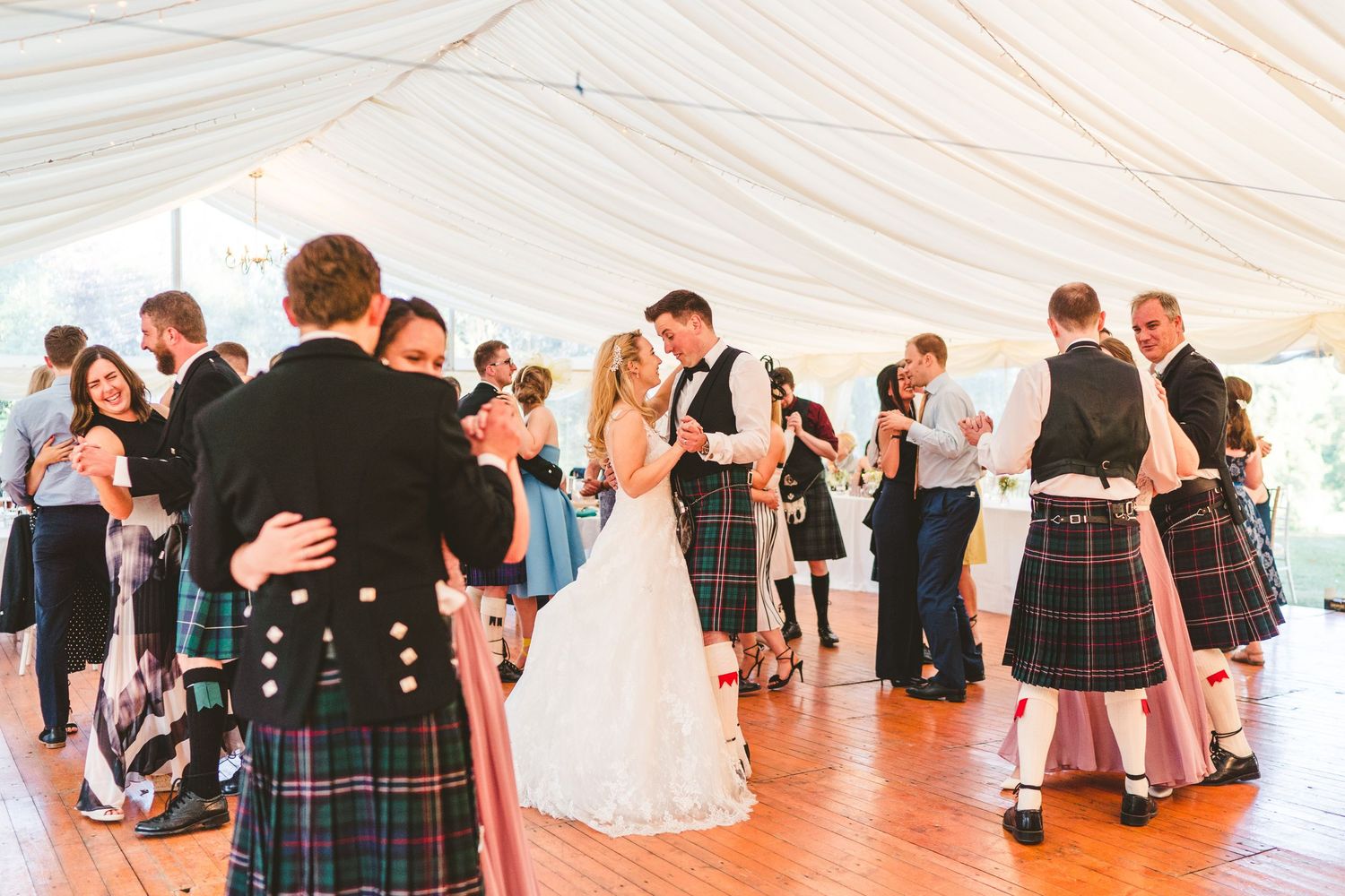 Wedding guests in traditional Scottish attire dancing at reception.