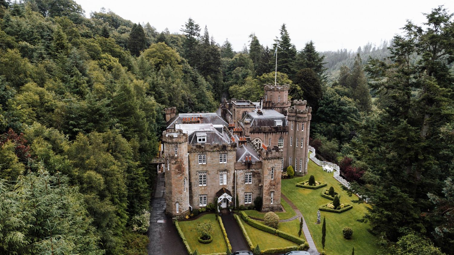 Panoramic view of a historic castle and gardens with lush green trees surrounding the stone architecture.