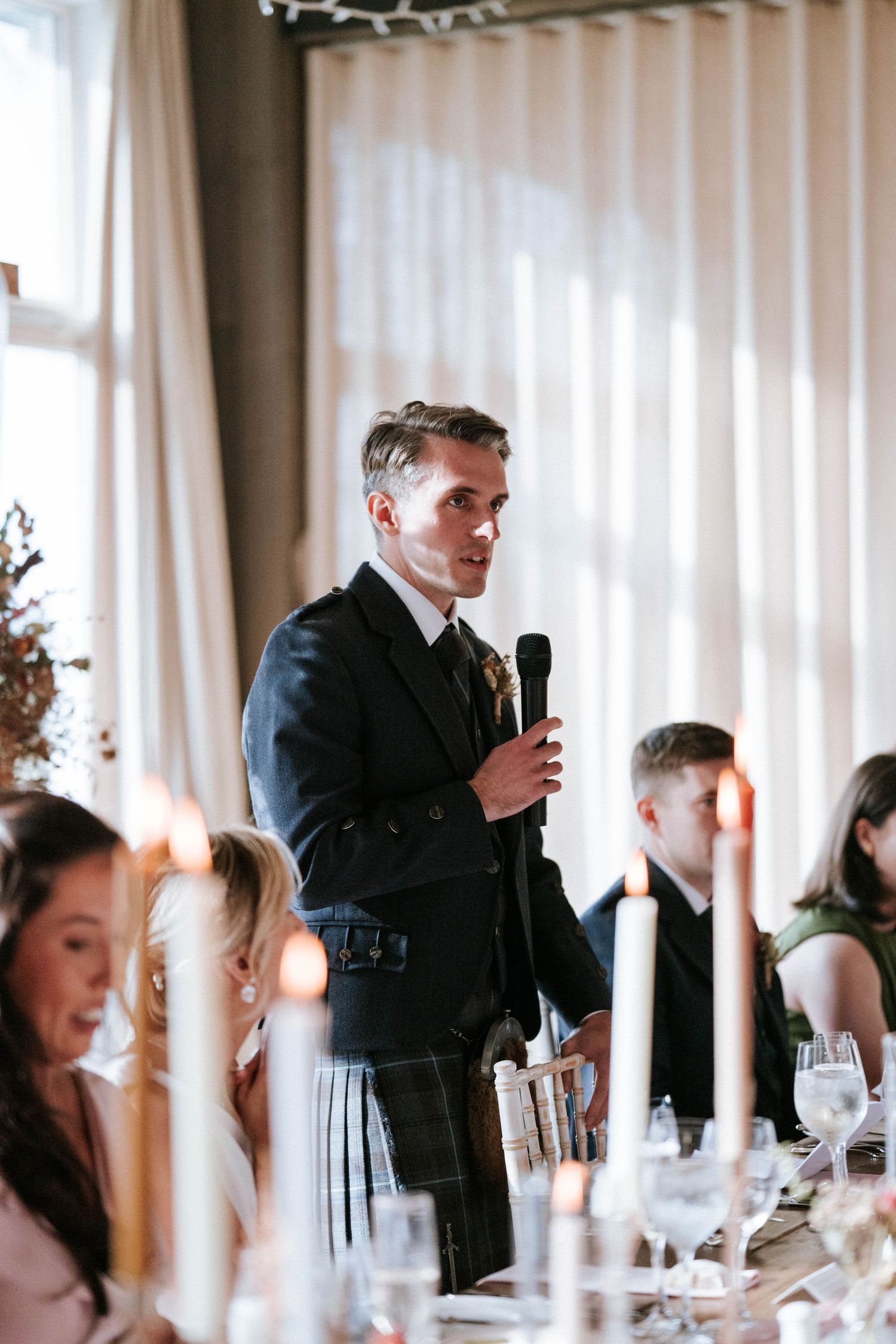Speaker giving wedding toast at elegant candlelit reception dinner.