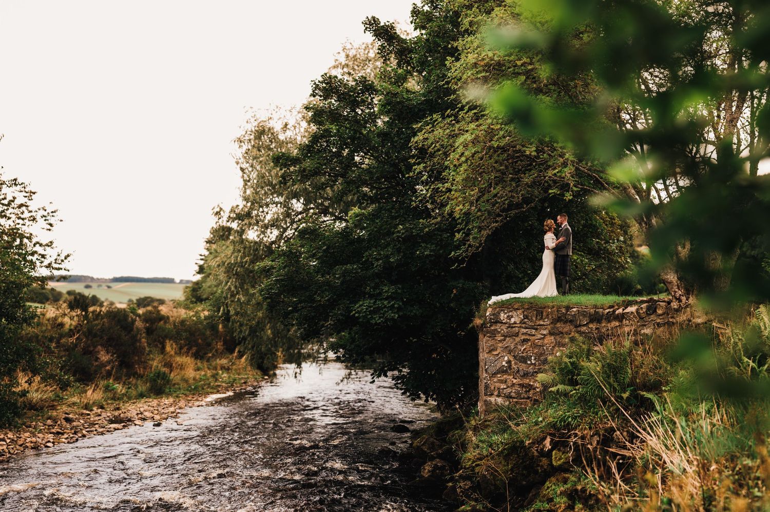 Scenic waterfront landscape with stone walls and trees at sunset creating a romantic outdoor setting.