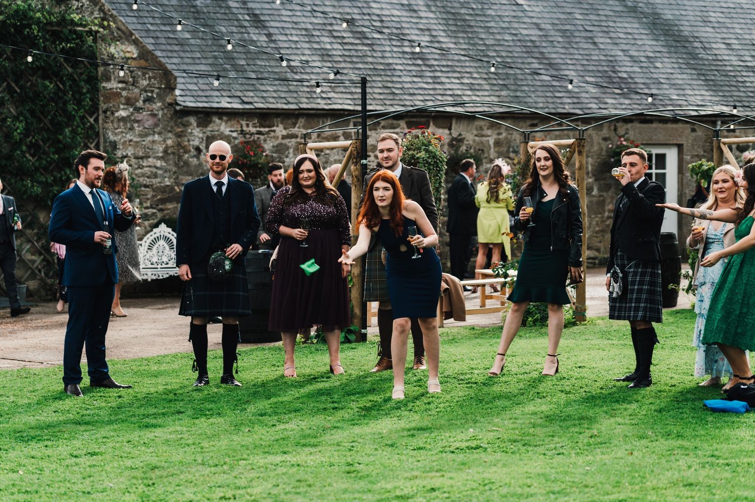 Wedding guests gathered on a lush green lawn outside a stone building during an outdoor ceremony.