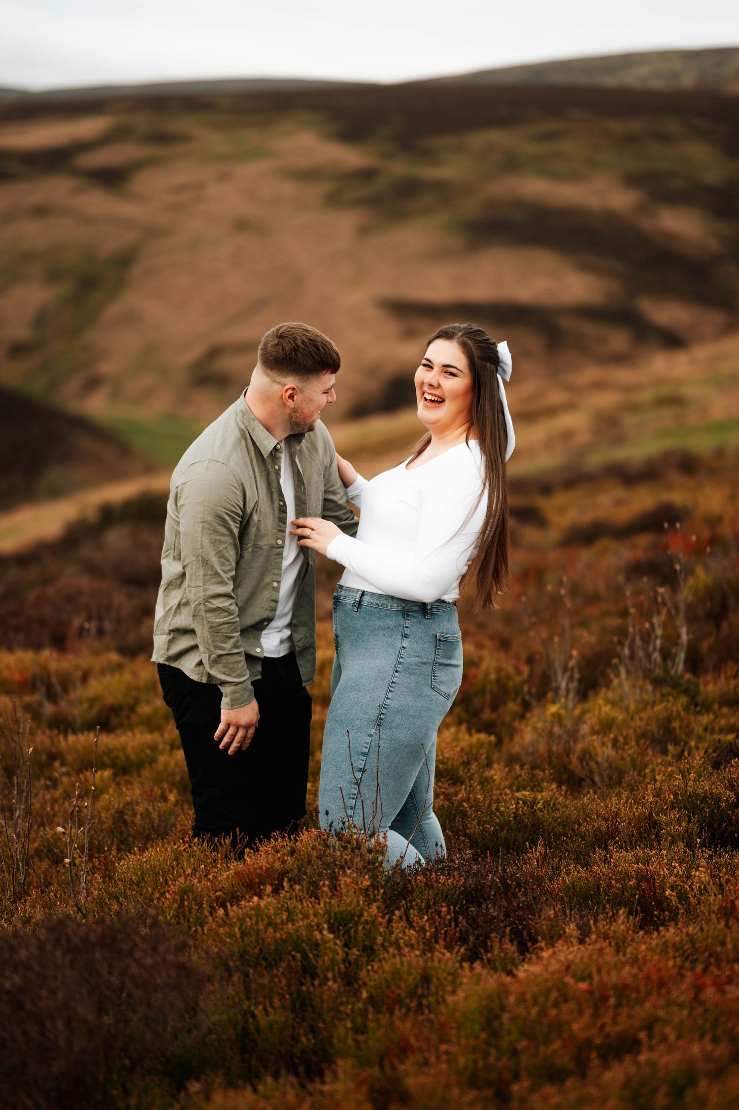 A couple shares a joyful moment together while standing in a field of heather during golden hour.