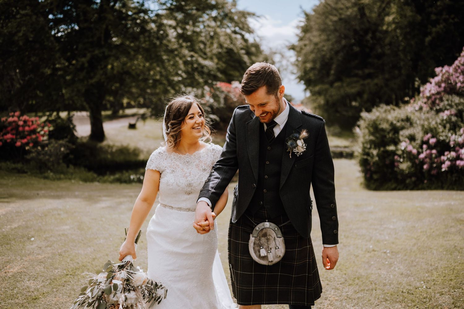 A sunny garden wedding portrait featuring Scottish highland dress and a flowing white gown.