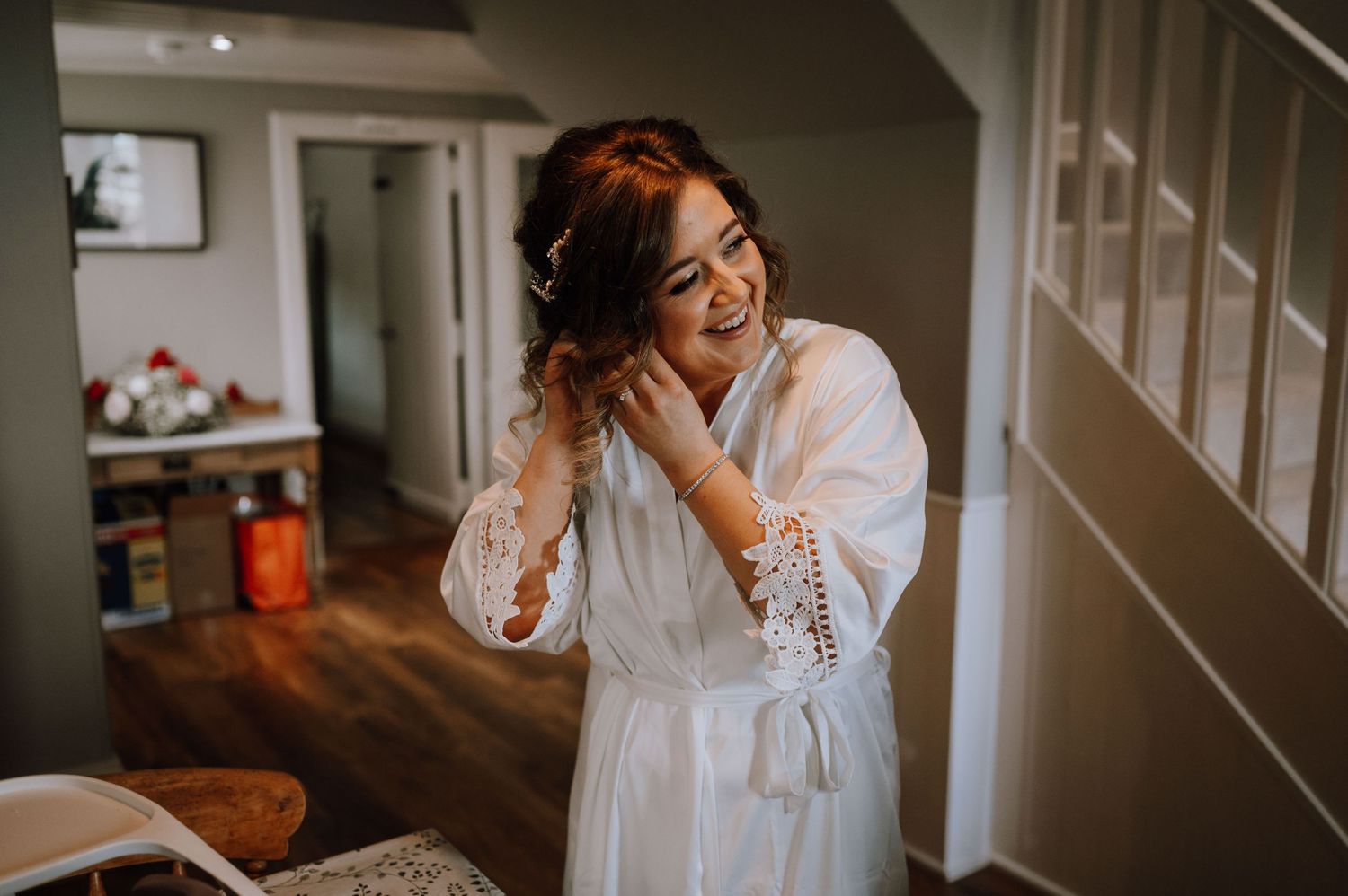 A candid morning moment showing a person in a white lace robe laughing while getting ready indoors.
