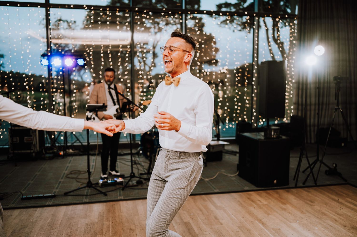 A person in white attire dances energetically on a wooden floor with stage lights and musicians in the background.