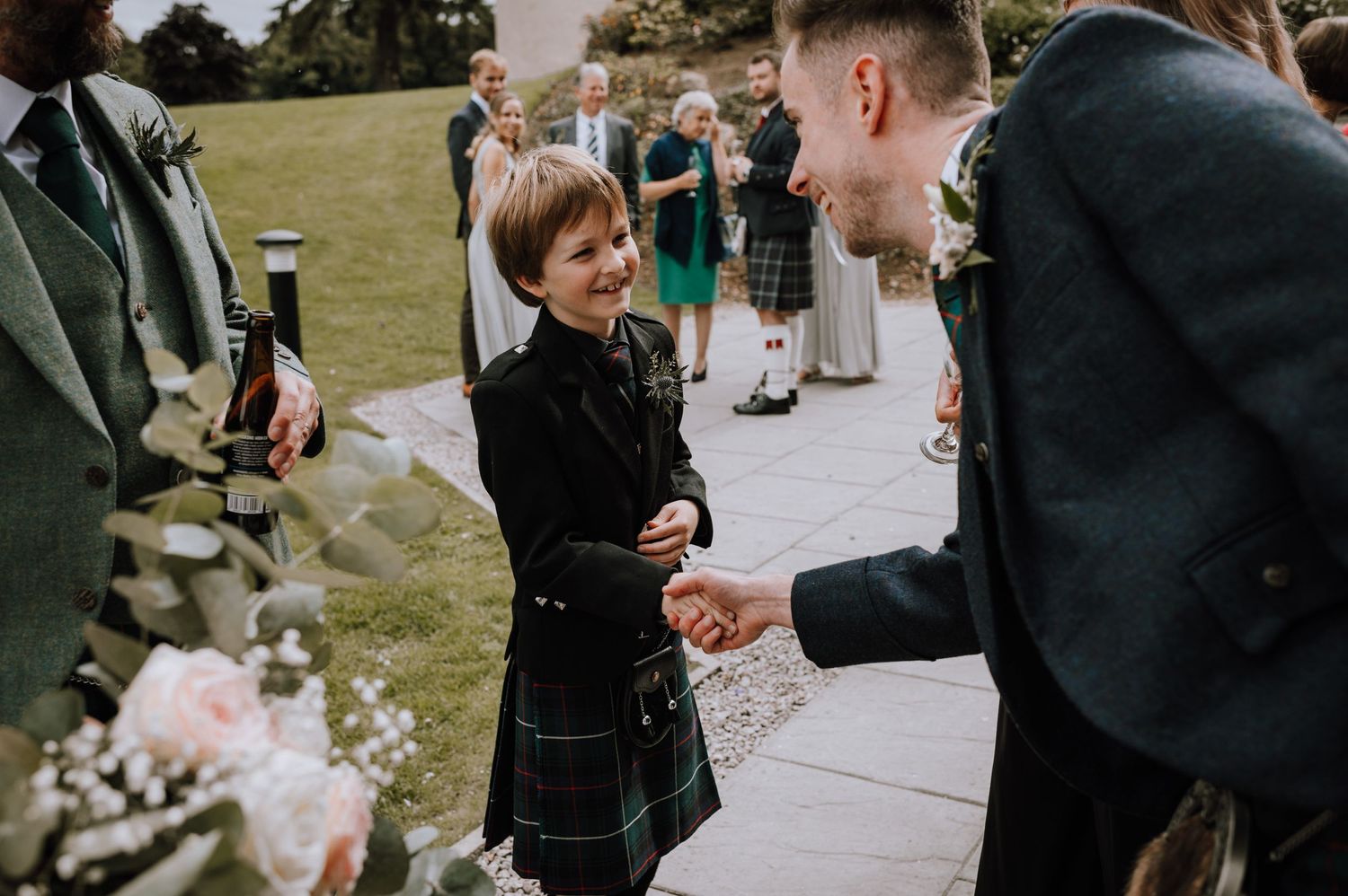 Joyful interaction between guests during a Scottish wedding reception on a grassy lawn.
