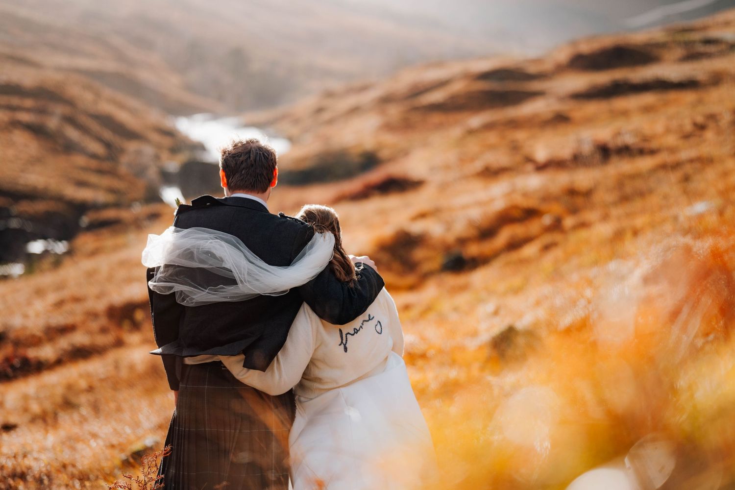A couple walks through a misty mountainous landscape with dramatic orange-tinted scenery at sunset.