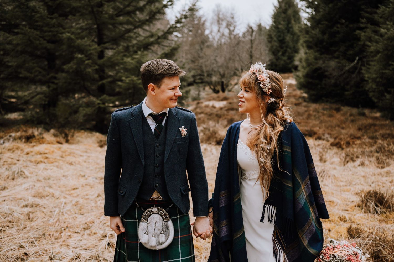Scottish wedding couple in traditional kilt and white dress share a romantic moment in the rugged Highland landscape.
