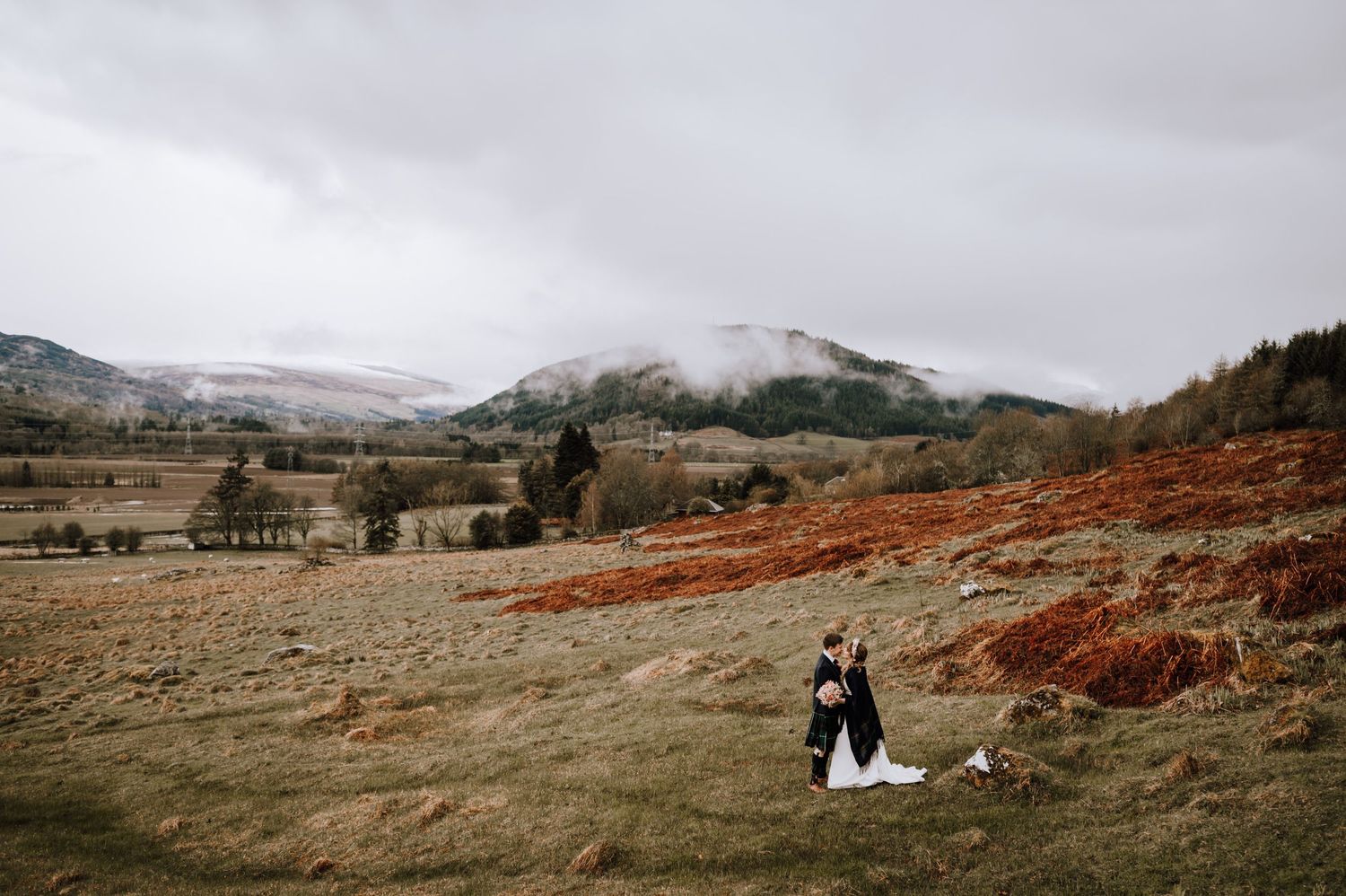 Wedding couple stands in misty Scottish Highland landscape with mountains in background.
