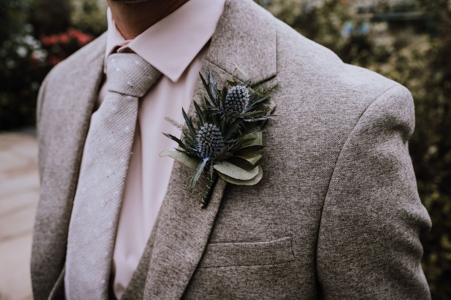 Close-up of a light gray suit jacket with a thistle boutonniere and silver tie.