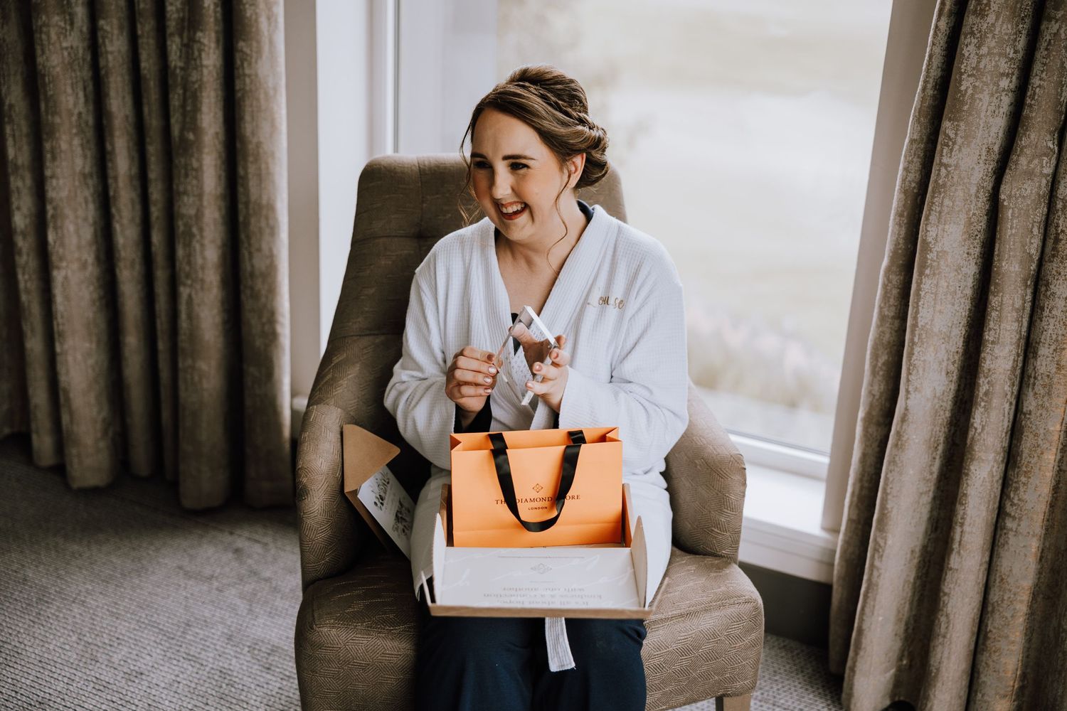 Person sitting in armchair opening an orange shopping bag with excited expression.