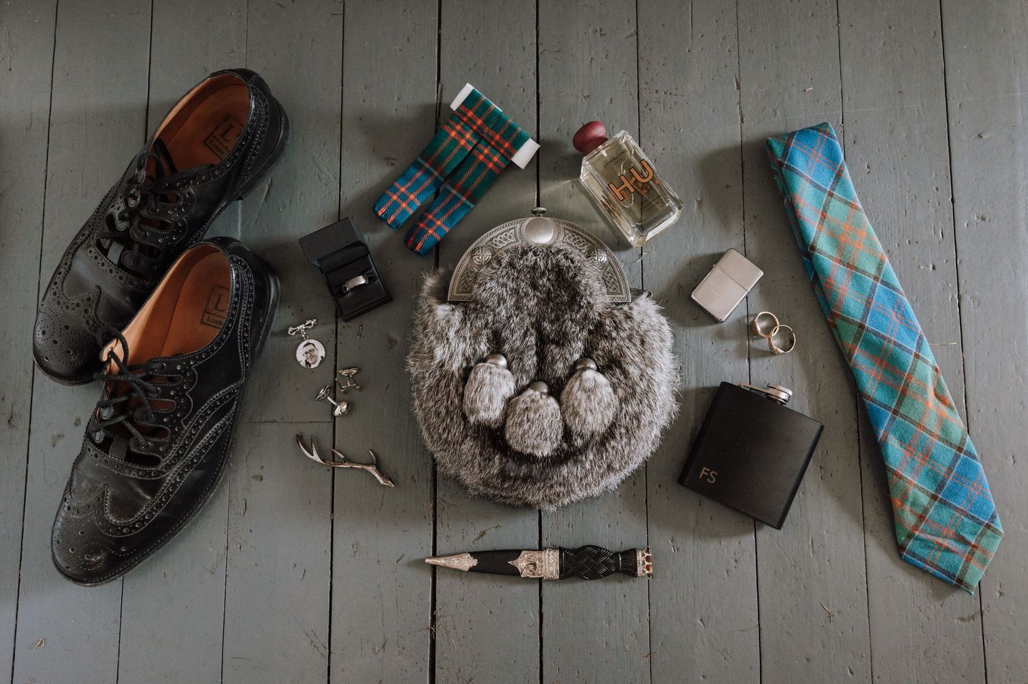Styled wedding details including shoes, tie, watch and accessories arranged on grey wooden flooring.
