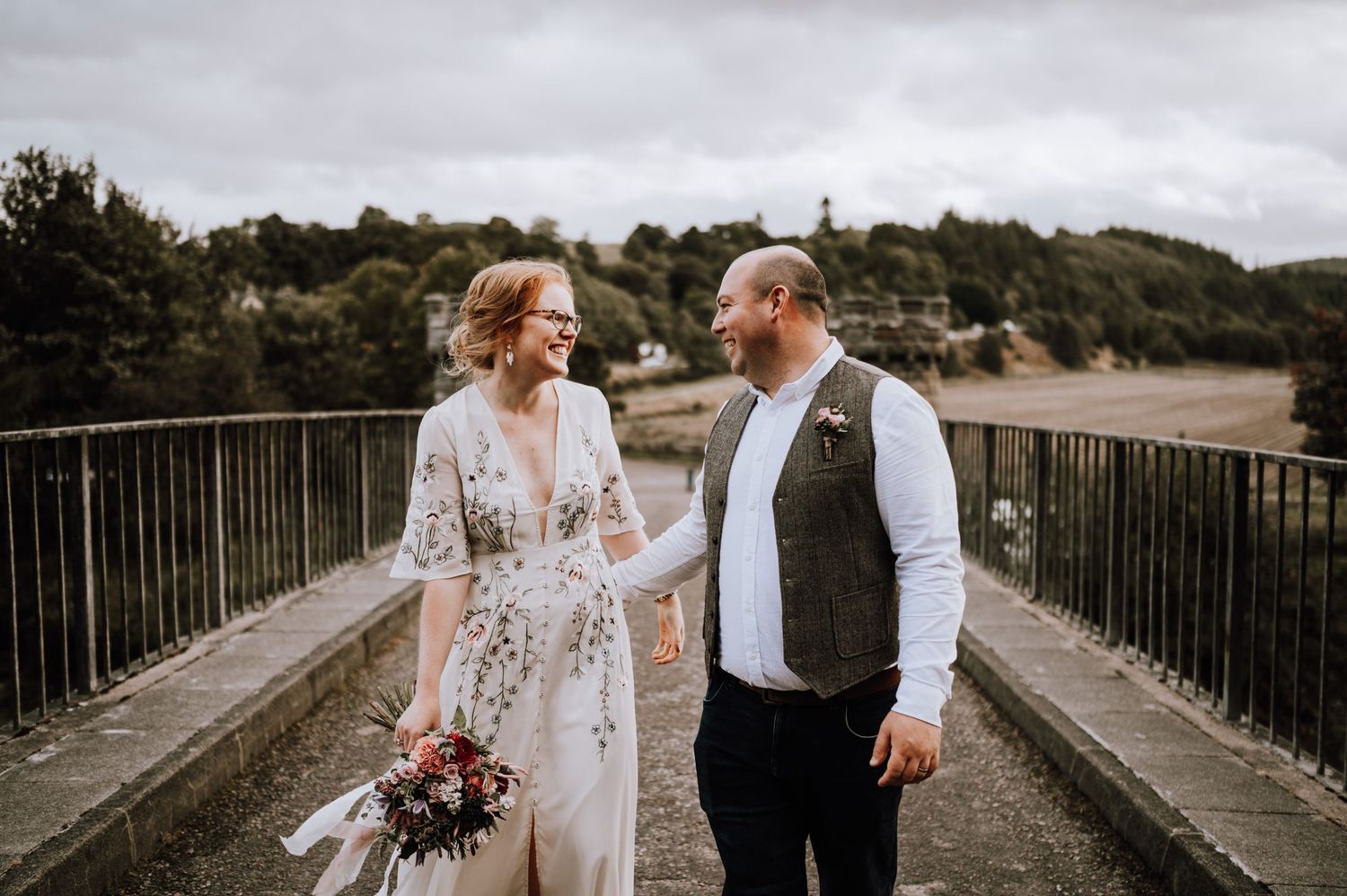 A romantic wedding couple shares a tender moment on a stone bridge surrounded by autumn foliage.