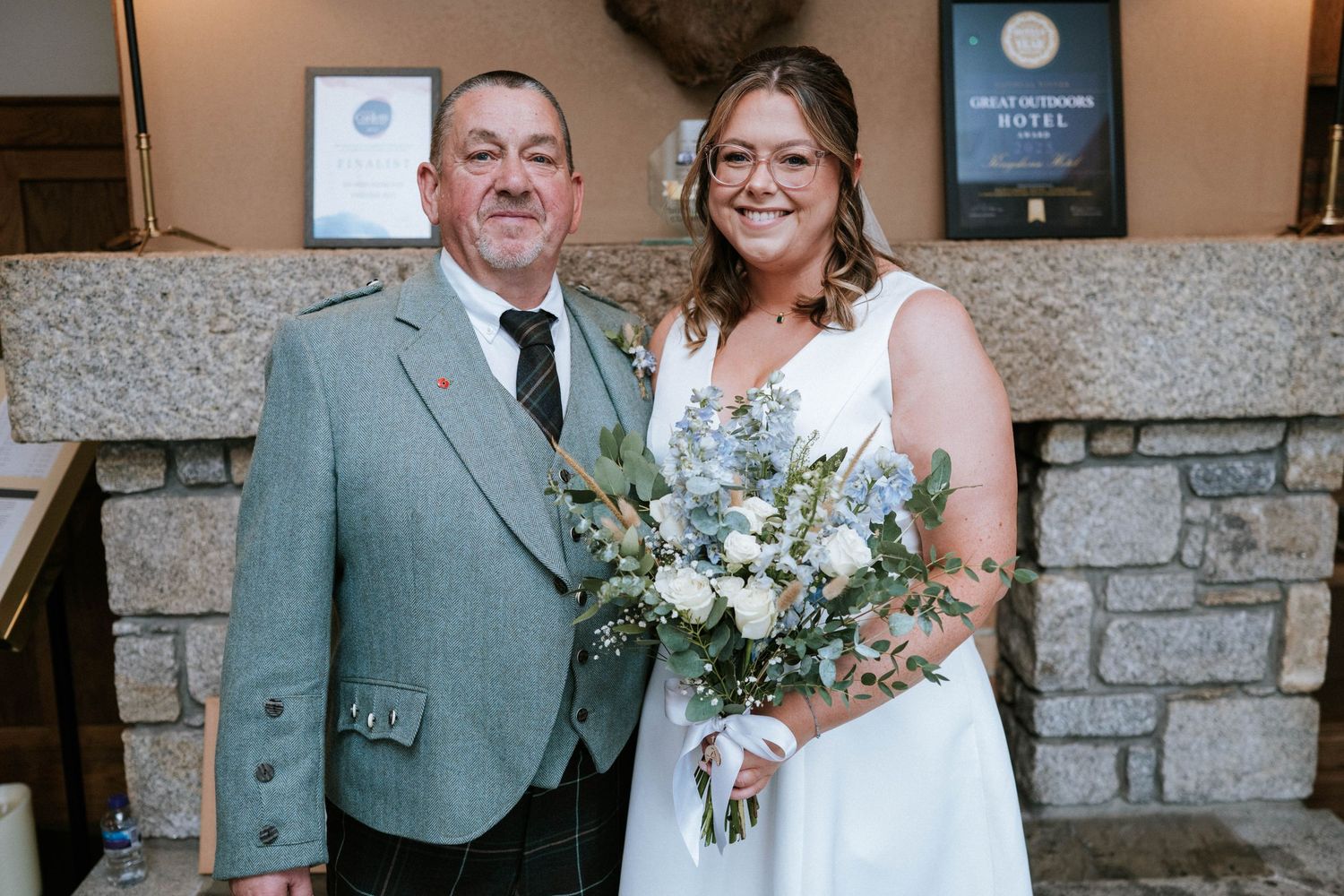 A bride in white holds a blue and white bouquet while posing with someone in a light gray suit.