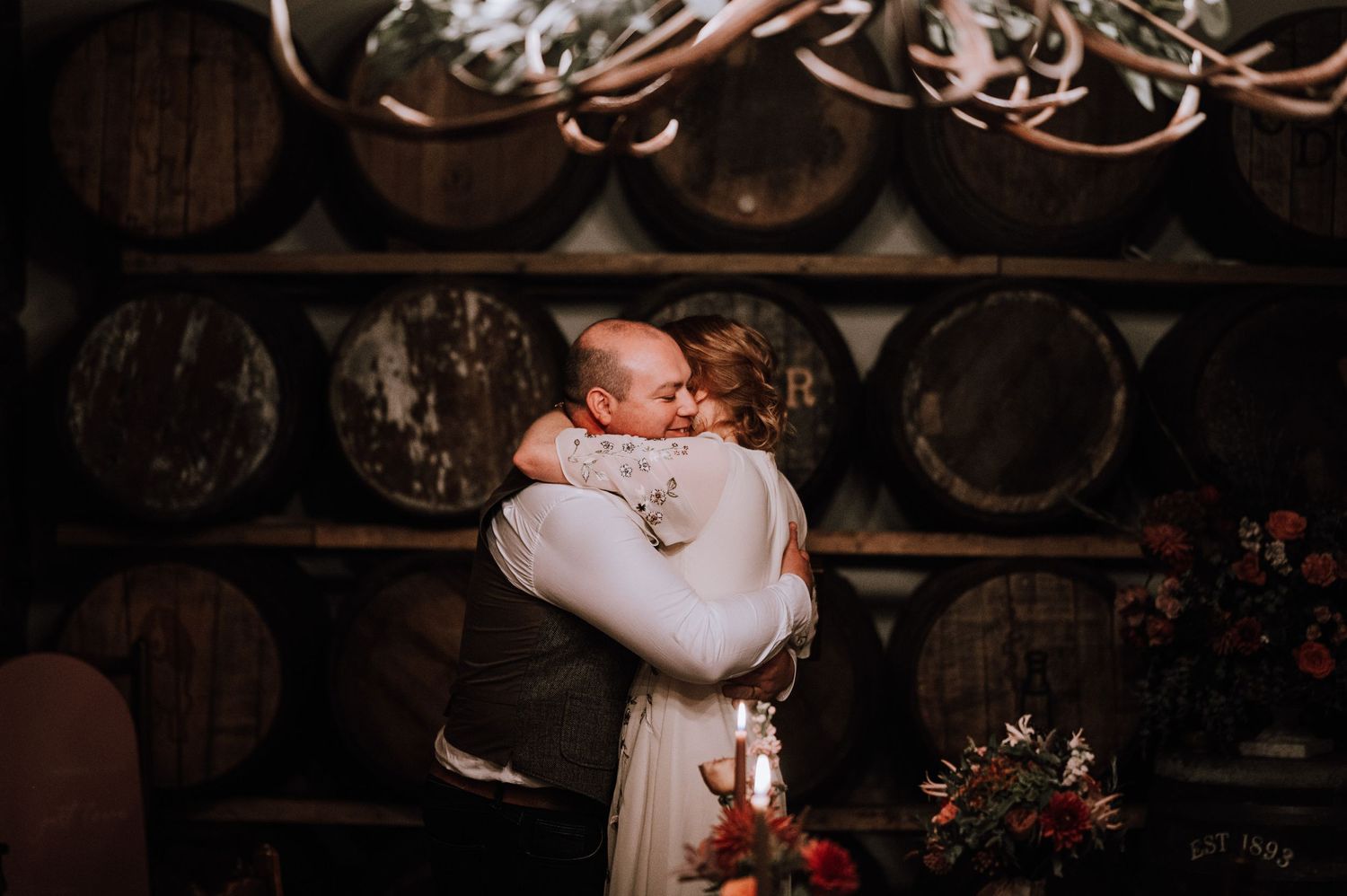 Intimate embrace captured in a rustic wine cellar setting.