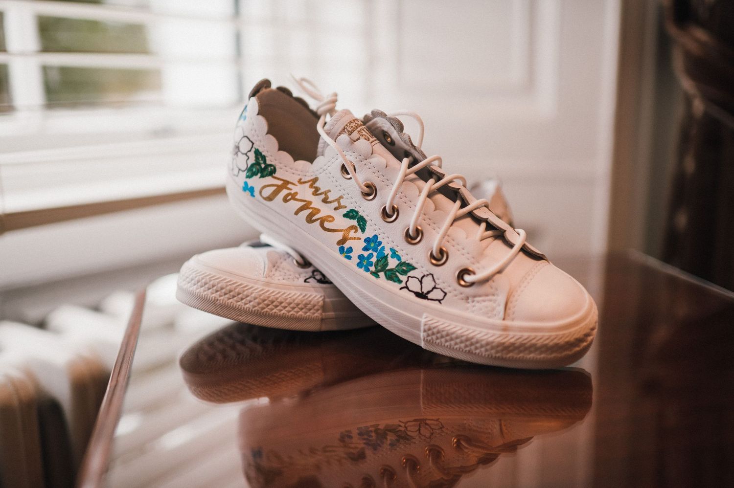 Pair of customized white sneakers with colorful floral patterns on a reflective surface.