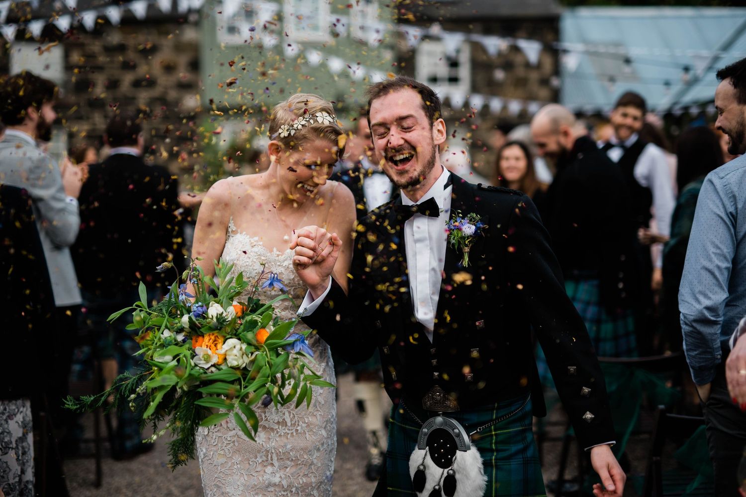 Wedding celebration with confetti toss at outdoor Scottish venue decorated with white bunting.