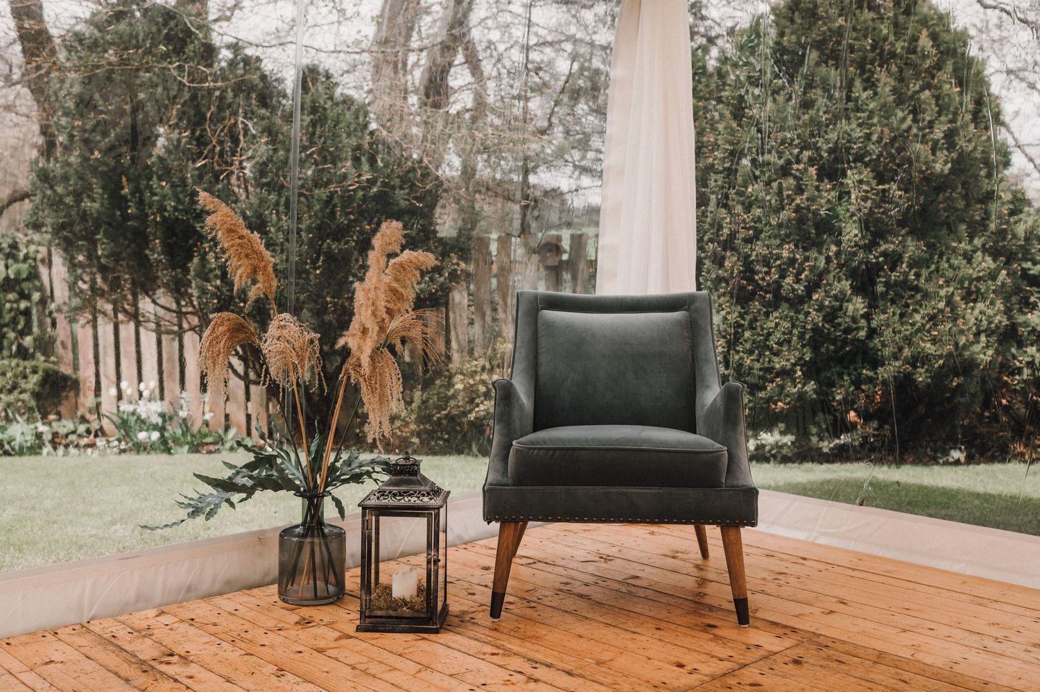 Modern black leather accent chair with dried flowers and lantern on wooden deck.
