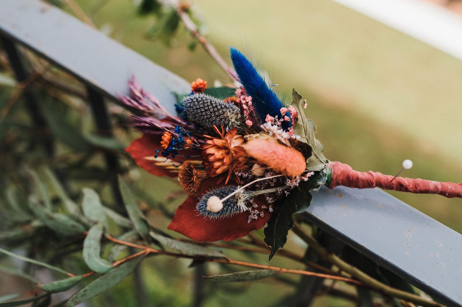 Artistic wedding bouquet with blue feathers and dried flowers in natural lighting.