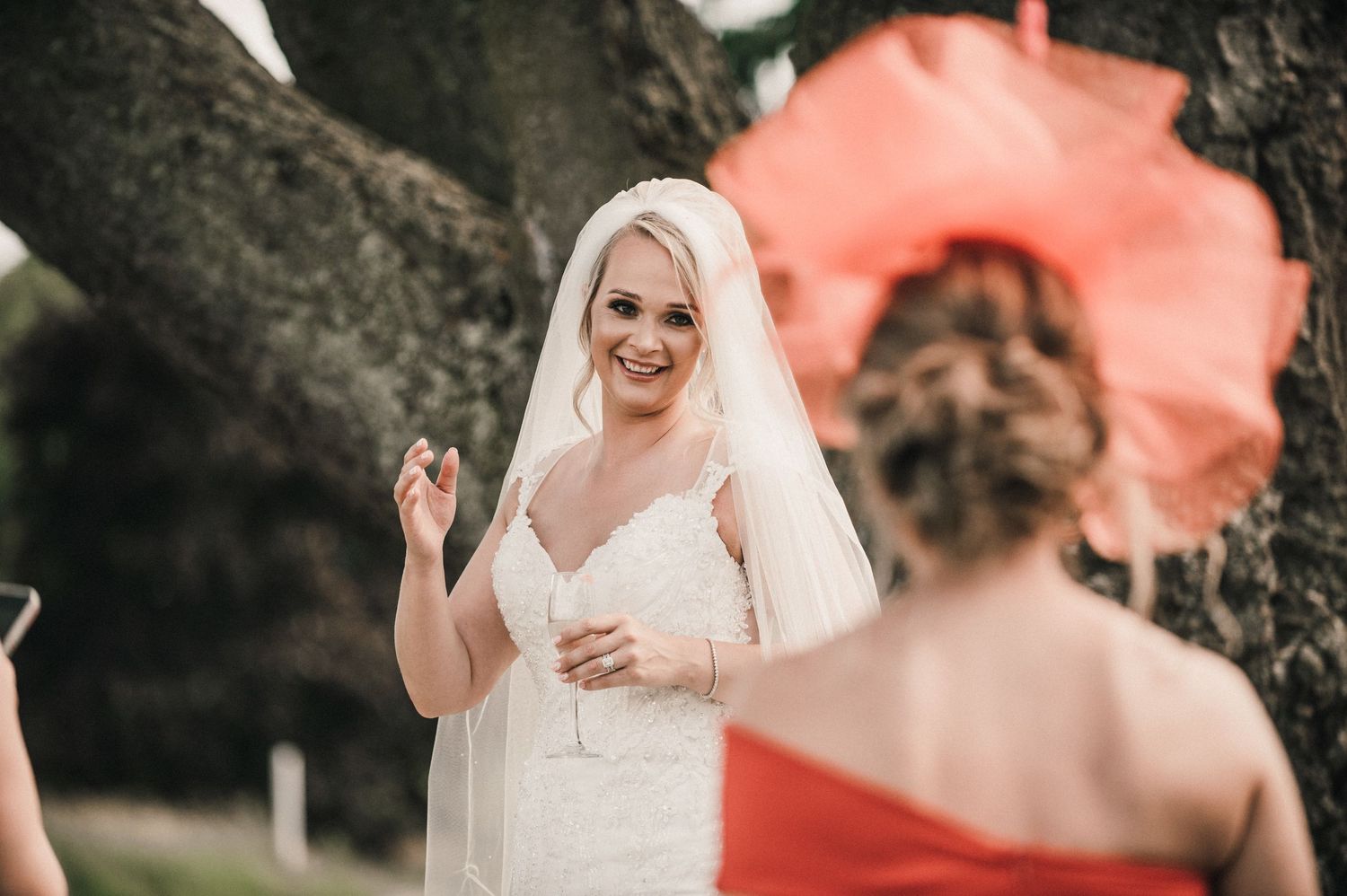 A wedding scene with a bright coral parasol backdrop in soft focus.