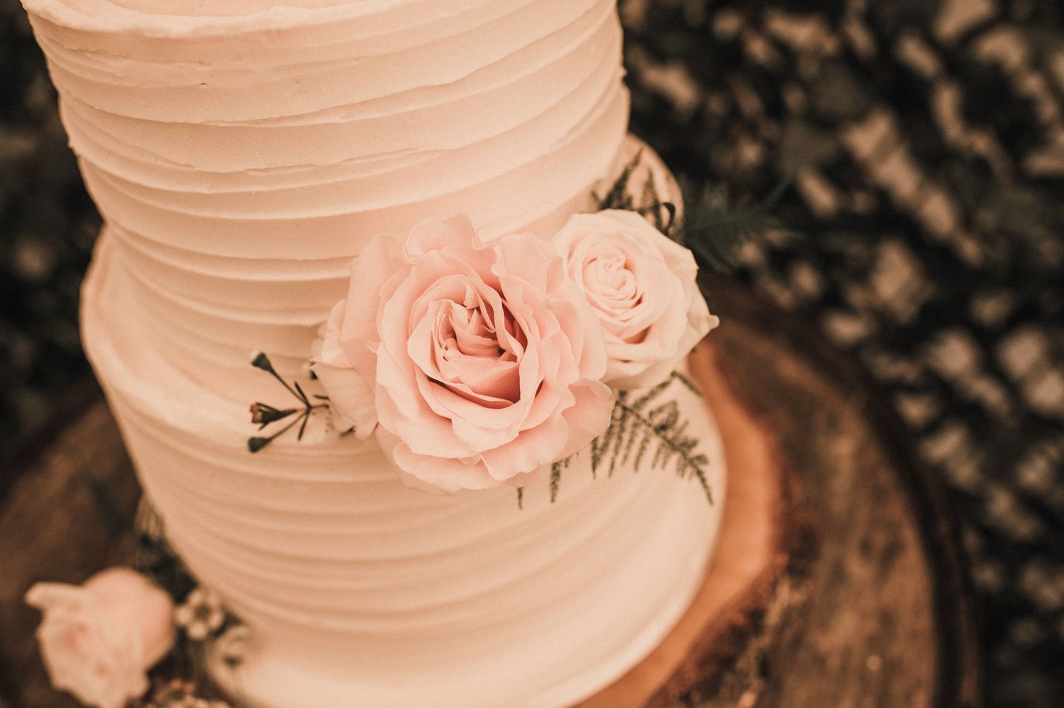 Close-up of white wedding cake decorated with blush pink roses and textured frosting.