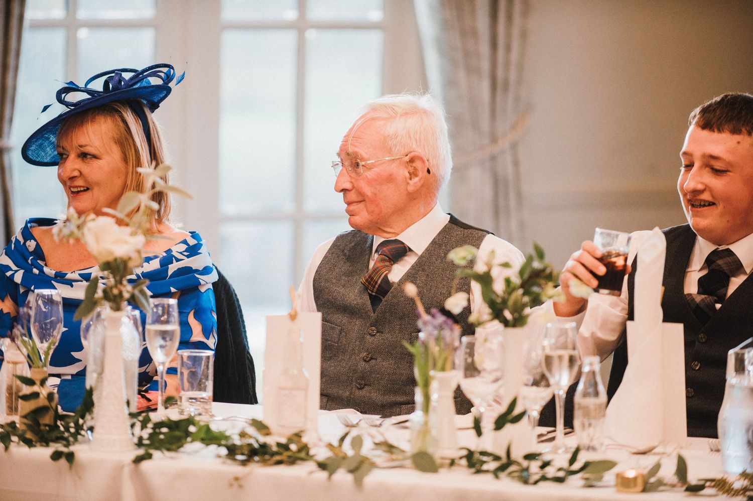 Wedding guests laugh and celebrate at an elegant reception dinner table decorated with candles and floral arrangements.
