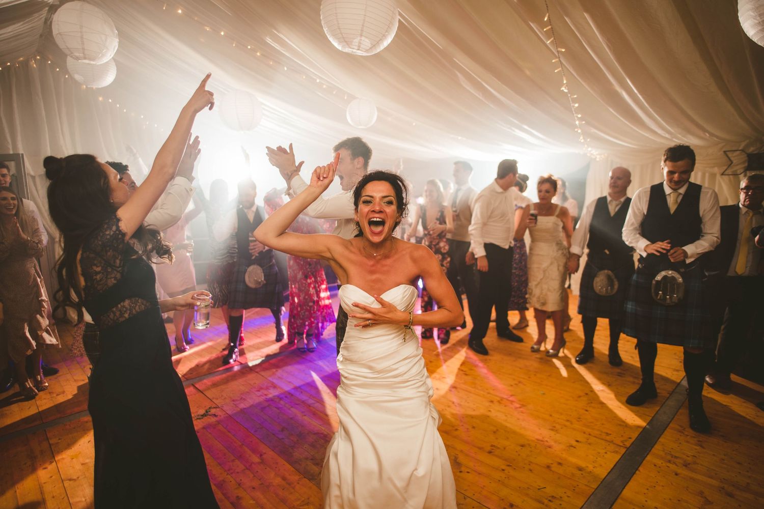 A bride dances joyfully surrounded by party guests at a wedding reception.