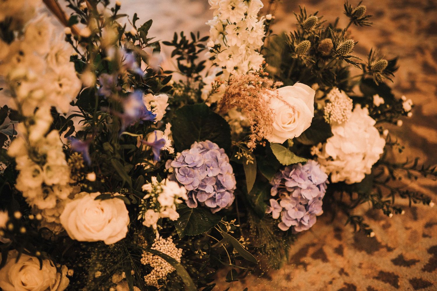 Close-up of wedding floral arrangement with purple hydrangeas and white roses against warm lighting.