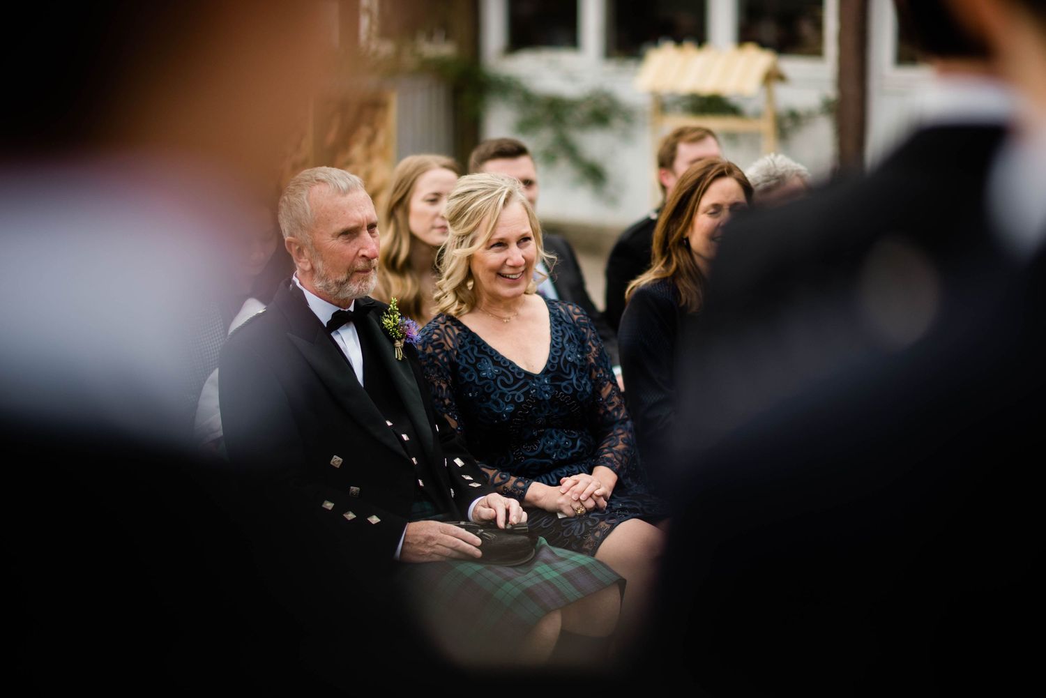 Wedding guests in formal attire seated during an outdoor ceremony.