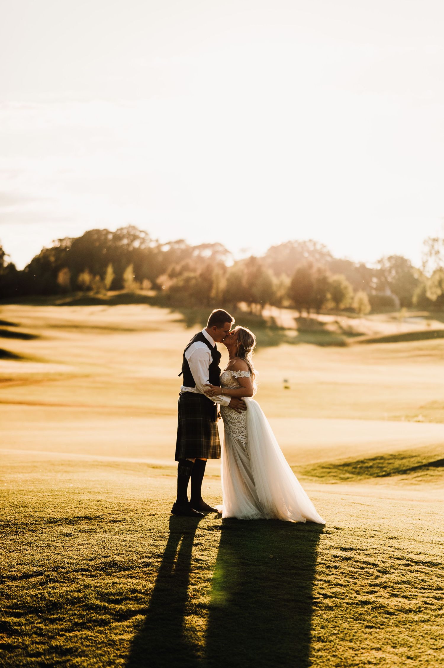 Newlyweds share an intimate moment at golden hour on a golf course.