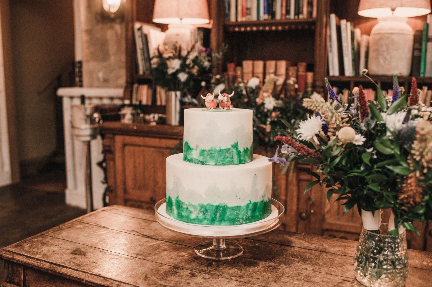 Elegant three-tier white wedding cake with green ribbon details displayed on wooden table.