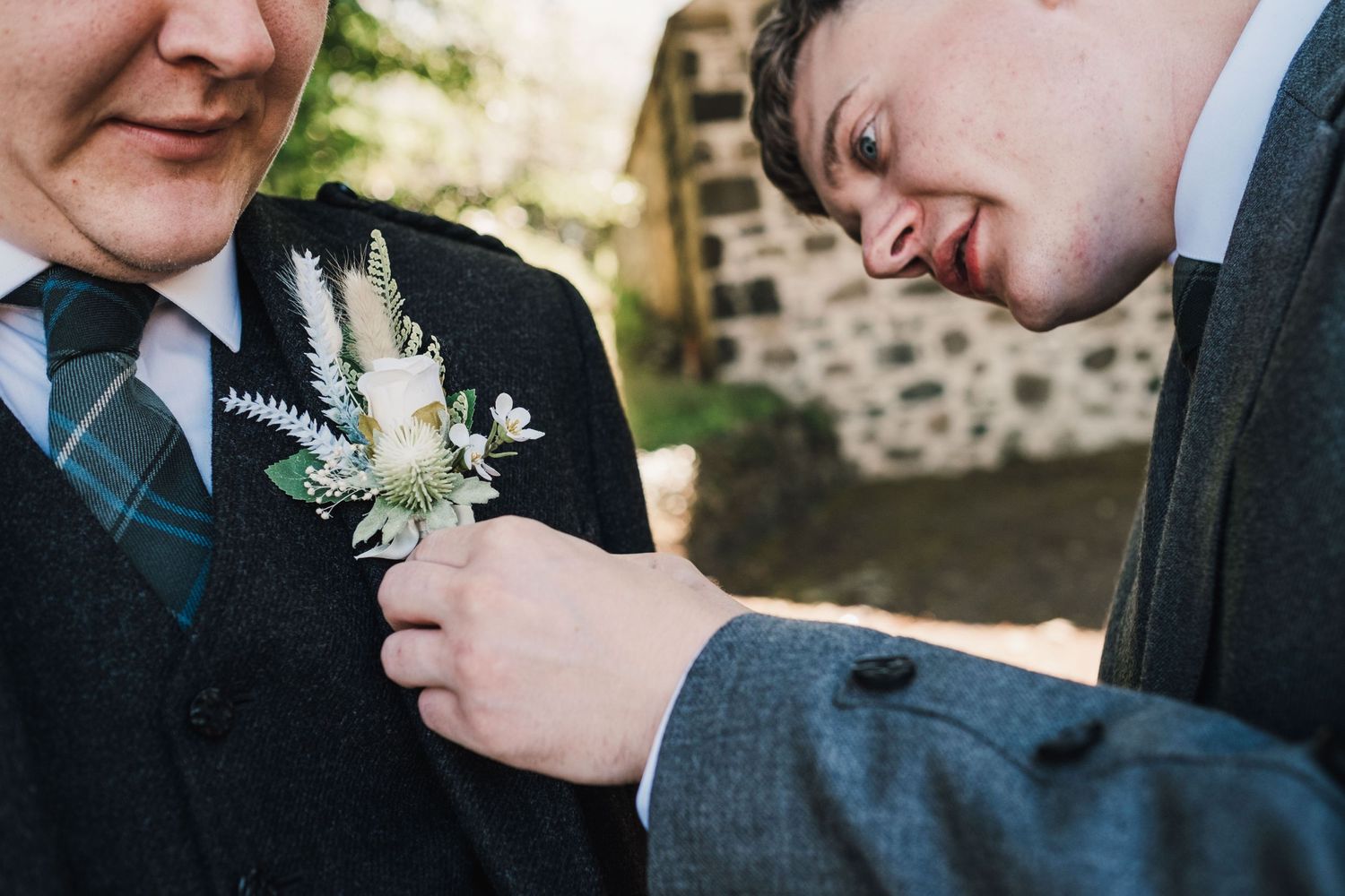 A close-up shot of someone pinning a white floral boutonnière to a formal suit jacket.
