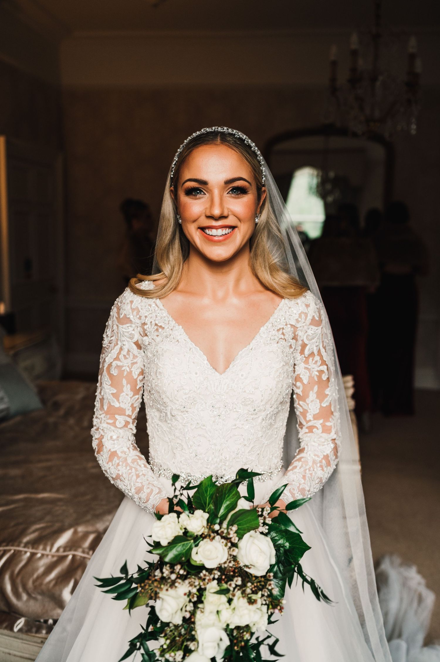 An elegant bride in a long-sleeve lace wedding gown holds a white and green bouquet.