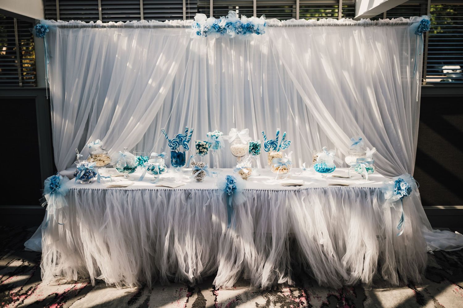 An elegant wedding reception table decorated with white tulle draping and blue floral accents against a dark backdrop.