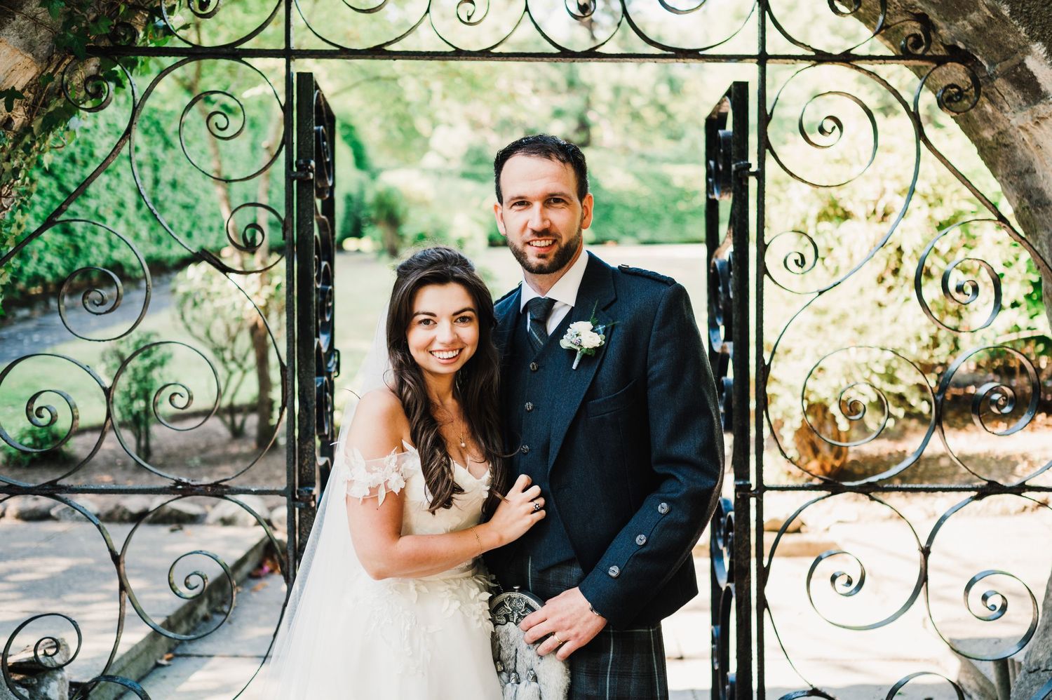 Elegant wedding portrait framed by ornate wrought iron garden gate.