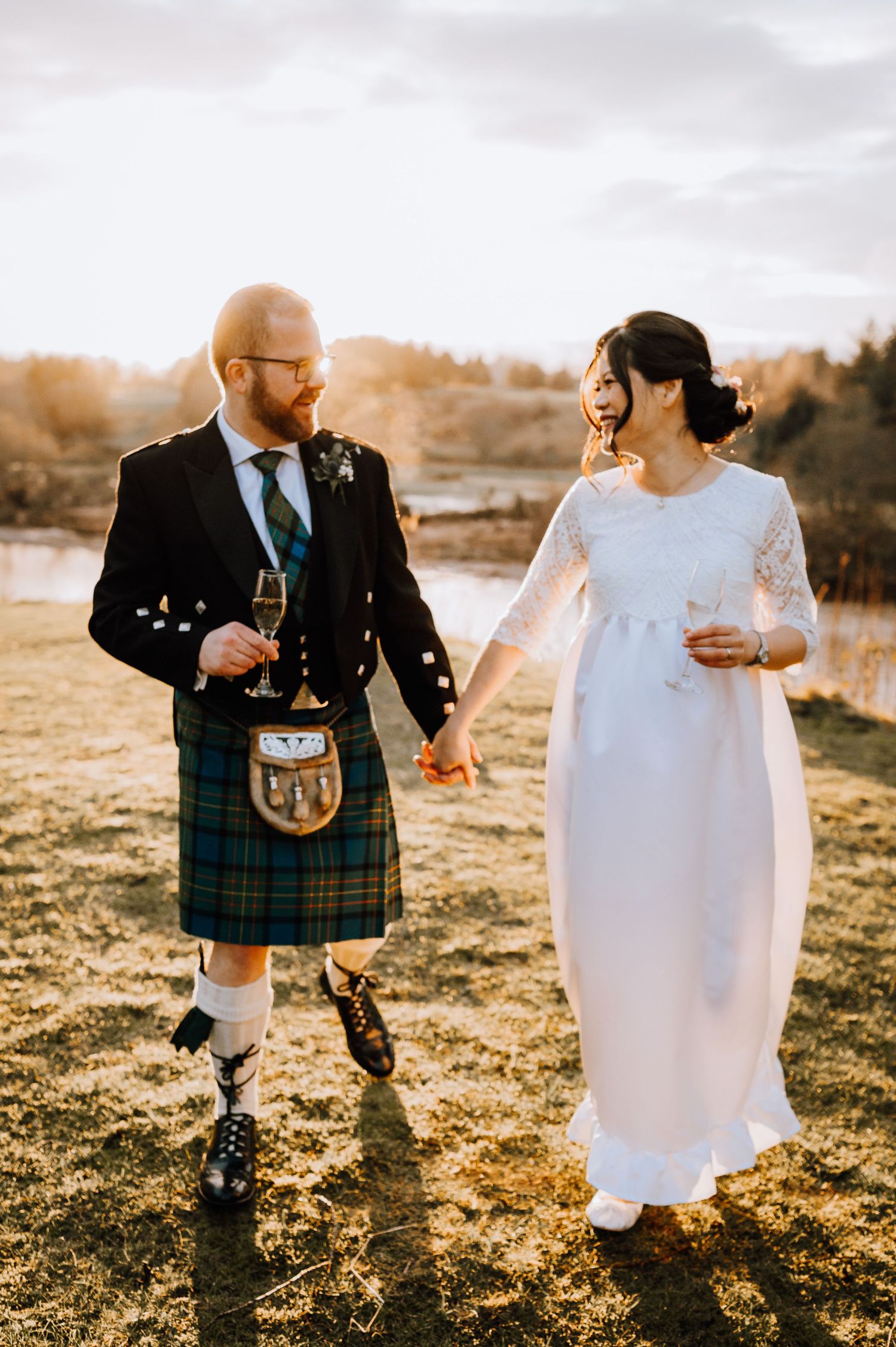 Sunset wedding portrait featuring traditional Scottish kilt and elegant white bridal gown.