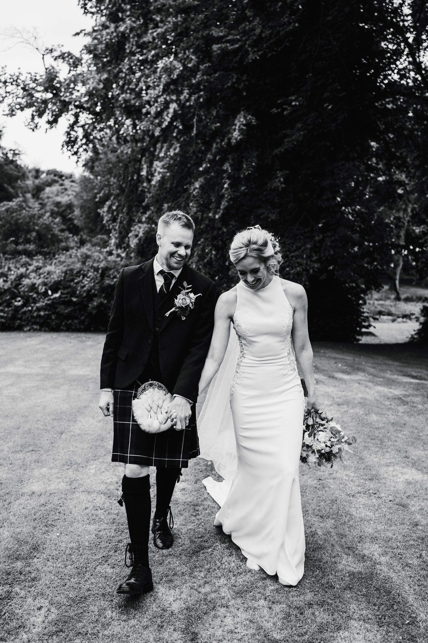 Black and white portrait of couple walking hand in hand at Scottish wedding venue.