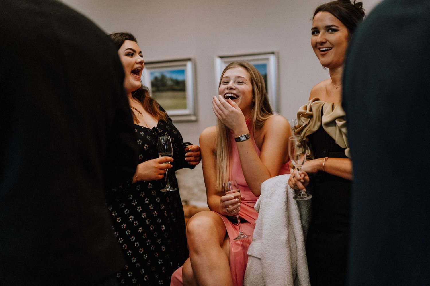 A group of friends laugh and share drinks while sitting together at a social gathering.