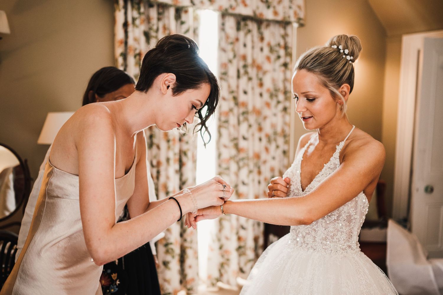 Final adjustments being made to a detailed lace wedding gown before the ceremony.