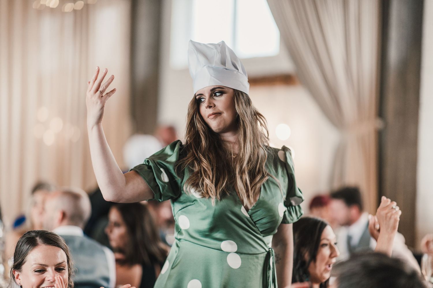 A guest in a green dress and chef's hat celebrates during a wedding reception.